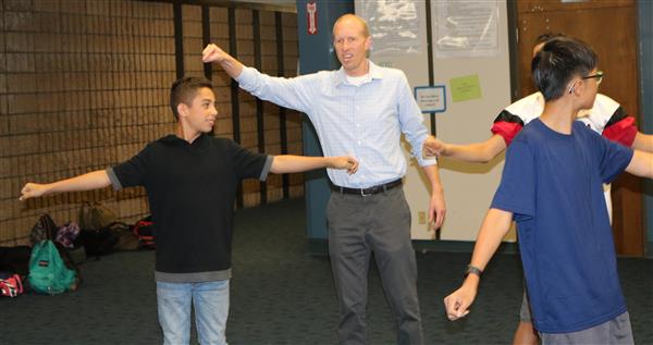 Teacher Ryan Brown shows four students how to space themselves apart by stretching out their arms to either side Teacher Ryan Brown shows four students how to space themselves apart by stretching out their arms to either side